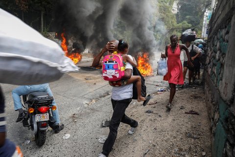 Mann trägt Kind über brennende Straße in Haiti.